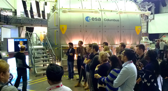 Londoner und Kölner Studierende zu Besuch im European Astronaut Centre der ESA. Studierende stehen im Kreis und schauen sich ein Trainingsgerät für Astronauten an.